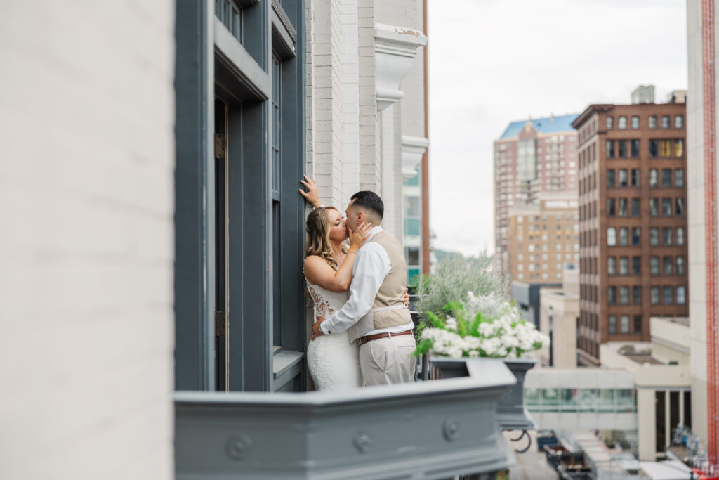 A bride and groom kissing on the balcony of The Tea Room in Des Moines before their wedding reception photographed by Claire Katan Creative.
