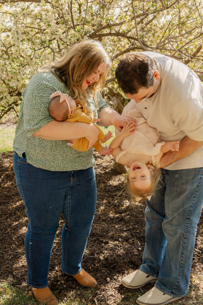 Spring family photos with parents, a newborn, and a toddler at Omaha's OPPD Arboretum surrounded by blooming flowers.