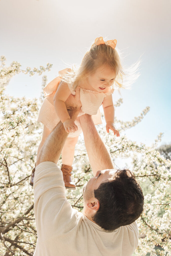 Spring family photos with parents, a newborn, and a toddler at Omaha's OPPD Arboretum surrounded by blooming flowers.