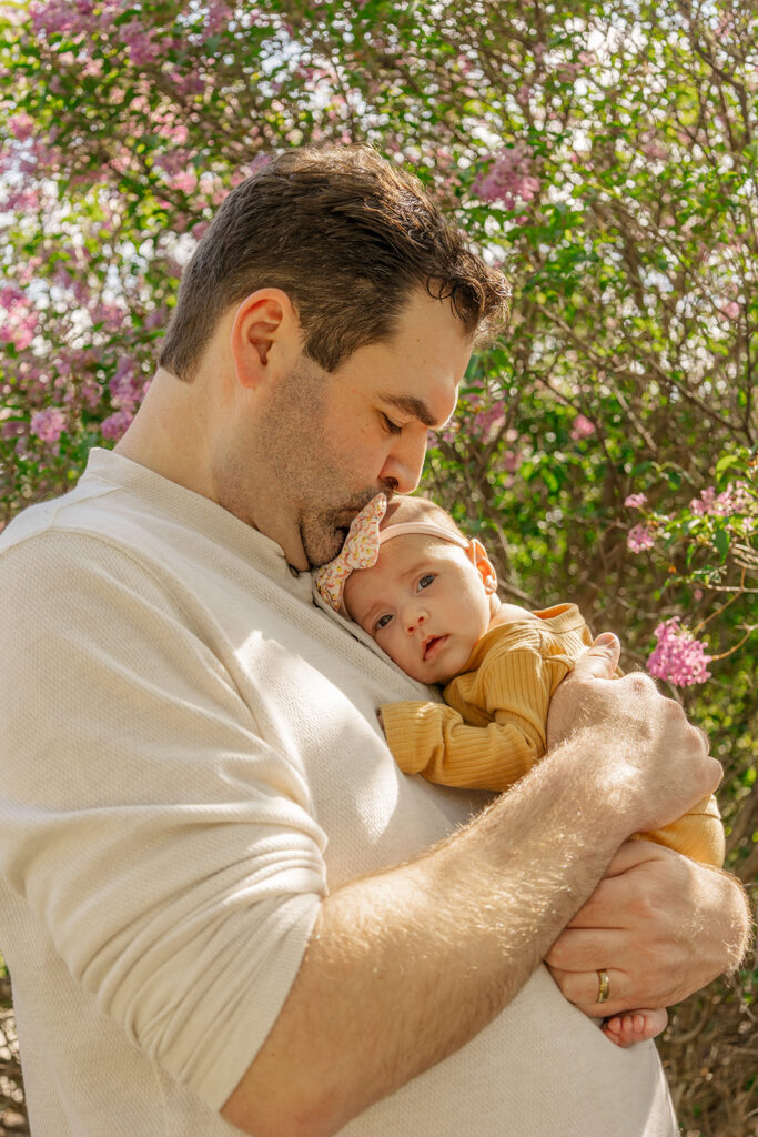 Spring family photos with parents, a newborn, and a toddler at Omaha's OPPD Arboretum surrounded by blooming flowers.