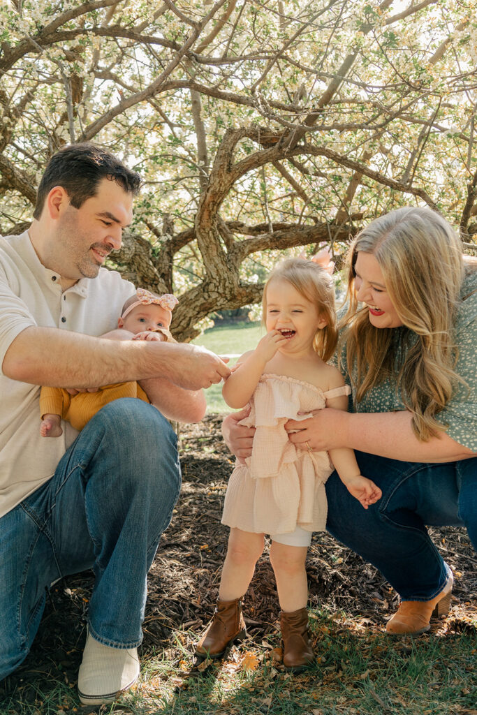 Spring family photos with parents, a newborn, and a toddler at Omaha's OPPD Arboretum surrounded by blooming flowers.