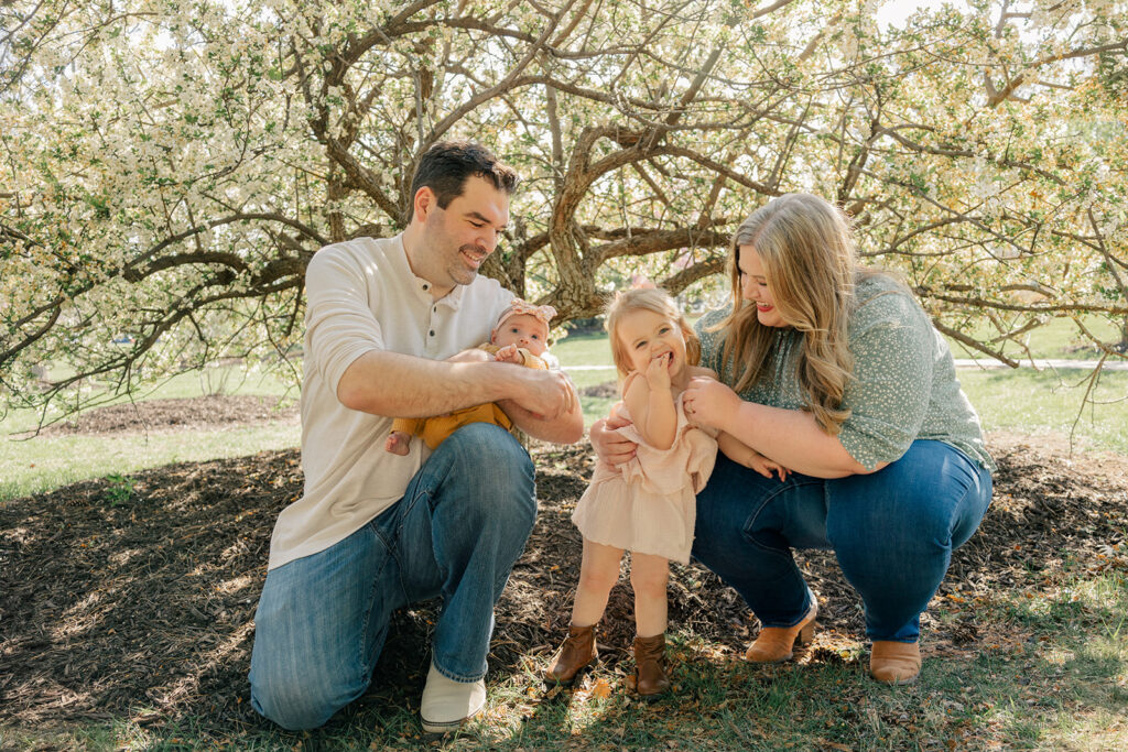 Spring family photos with parents, a newborn, and a toddler at Omaha's OPPD Arboretum surrounded by blooming flowers.